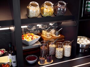 A buffet area with various food items, including a bowl of fruit salad, jars of nuts and seeds, and a bowl of red fruit compote. - B&B Hotel Wetzlar (Wetzlar)