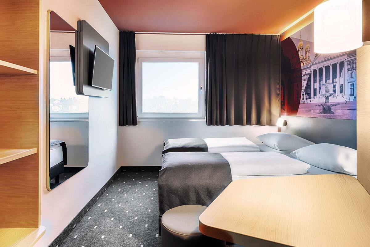 Een hotelkamer met een bed, een bureau, een stoel, een televisie en een raam met gordijnen.