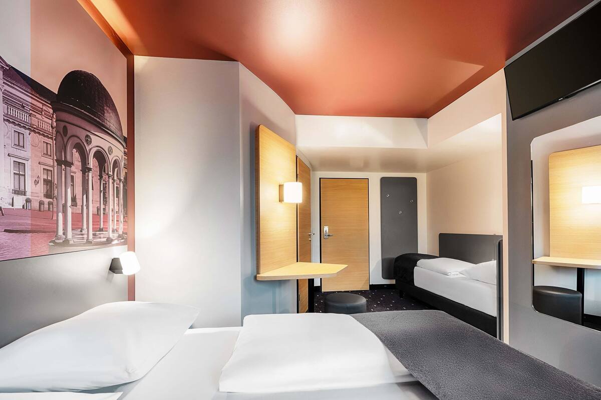 Een moderne hotelkamer met een bed, nachtkastjes, een bureau en een grote spiegel.