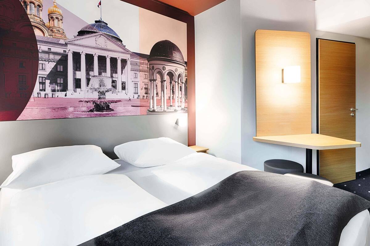 Een hotelkamer met een bed, een bureau en een wandlamp.