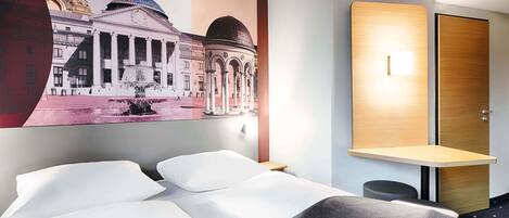 A hotel room with a bed, a desk, and a wall-mounted lamp.