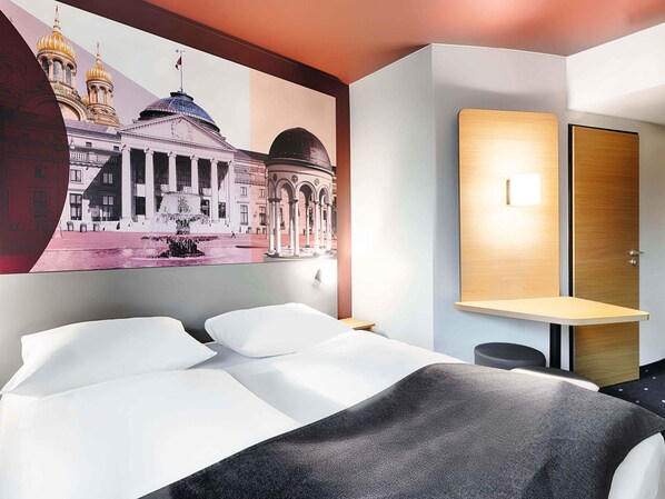 A hotel room with a bed, a desk, and a wall-mounted lamp. - B&B HOTEL Wiesbaden-Hbf (Wiesbaden)