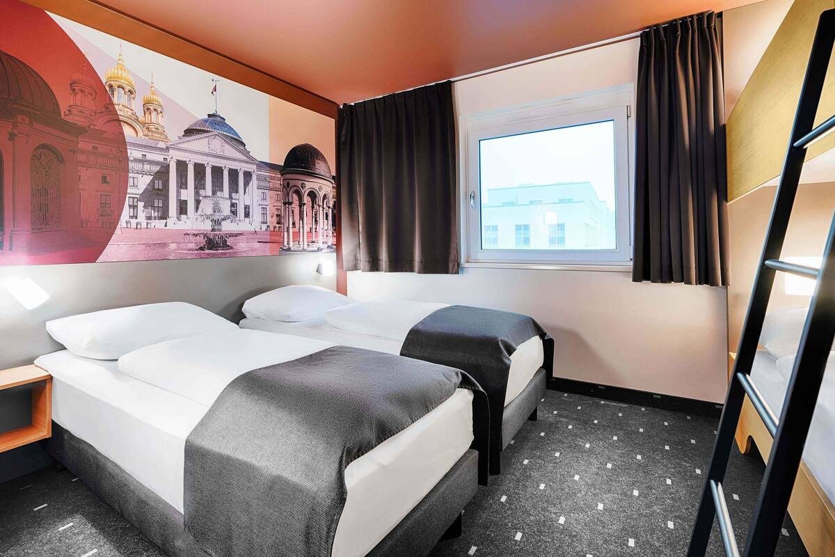 Een hotelkamer met twee bedden, een raam met gordijnen, een muurschildering en een ladder.