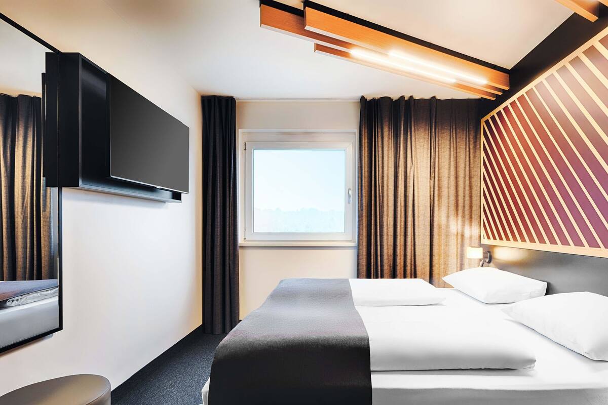 Een moderne hotelkamer met een bed, een flatscreen televisie, een raam met gordijnen en uitzicht op de omgeving.