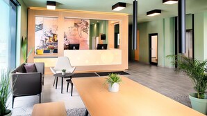 A modern reception area with a wooden reception desk, a large window, and a view of the interior. - B&B Hotel Wilhelmshaven (Wilhelmshaven)