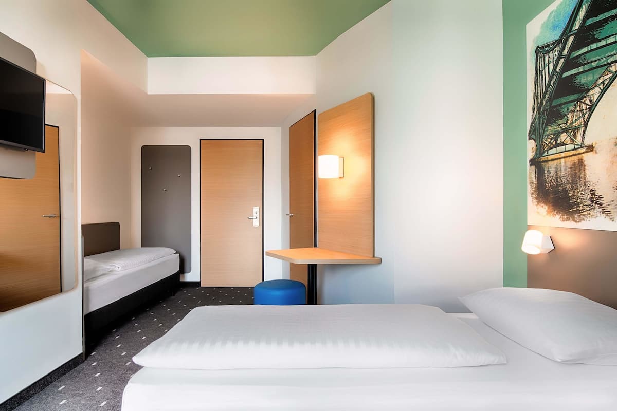 Une chambre d’hôtel avec un grand lit, un lit plus petit, un bureau et un téléviseur fixé au mur.