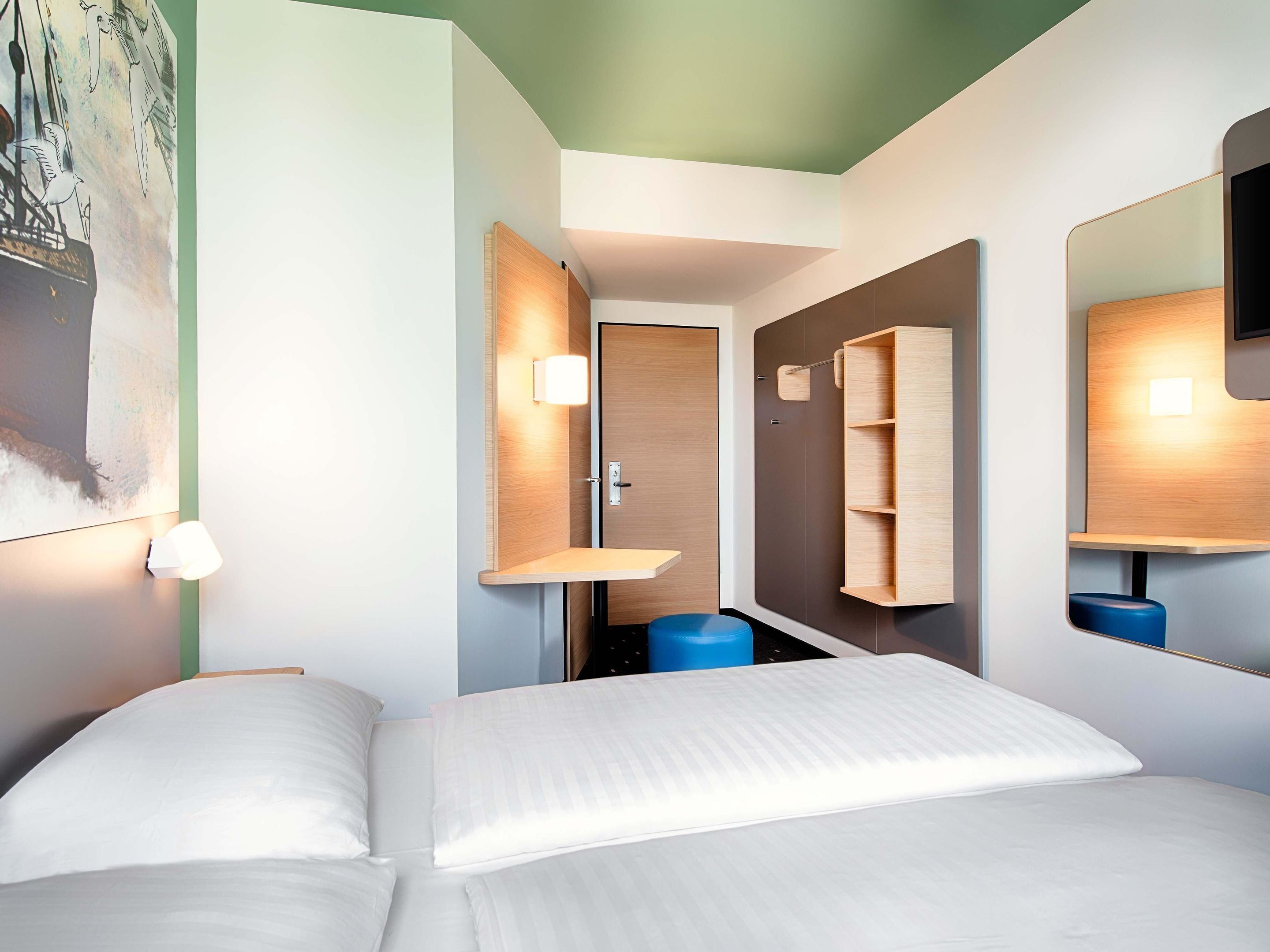 Et moderne hotelværelse med seng, skrivebord, stol, garderobeskab og spejl.