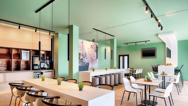 A modern restaurant with a long counter, multiple seating areas, and a large wall-mounted TV. - B&B Hotel Wilhelmshaven (Wilhelmshaven)