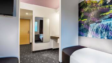 A hotel room with a bed, a TV, a bathroom with a mirror, and a wall with a waterfall painting.