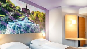 Quarto de hotel com duas camas, um grande mural de uma cascata, uma mesa de cabeceira de madeira e uma luminária fixada na parede.