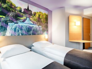 Hotelkamer met twee bedden, een groot wandkunstwerk van een waterval, een houten nachtkastje en een wandlamp.