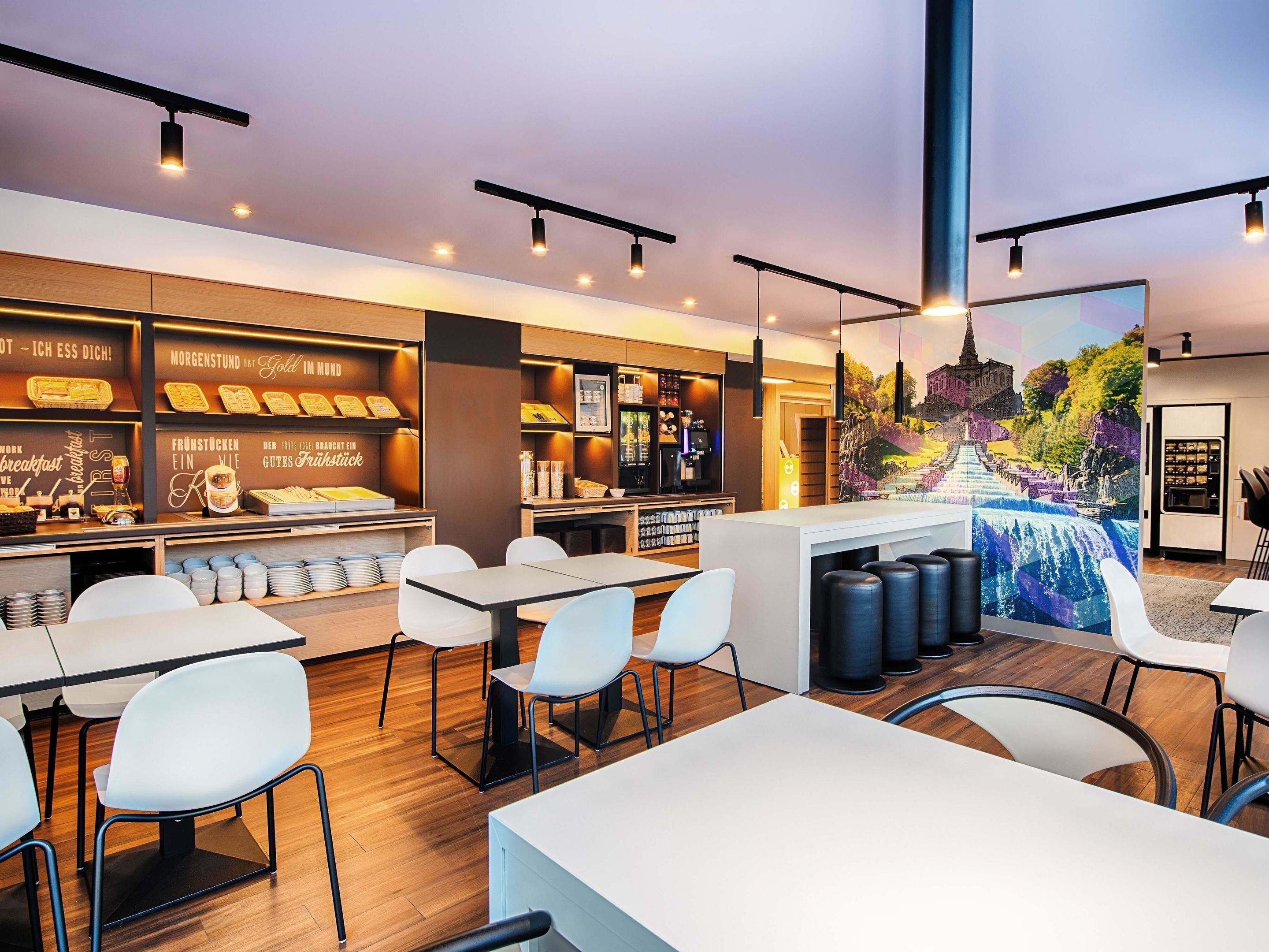 A modern cafe with a breakfast bar, seating area, and a mural.
