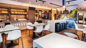 A modern cafe with a breakfast bar, seating area, and a mural. - B&B Hotel Kassel-Süd (Lohfelden)