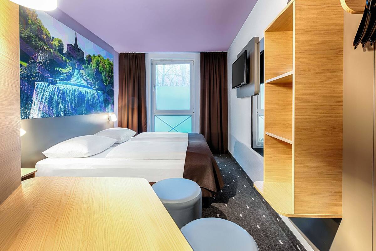 Ett hotellrum med en säng, ett skrivbord, en stol, en tv och en garderob.