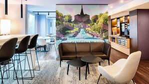 Quarto de hotel moderno com um grande mural de uma cascata, área de bar e espaço de estar com um sofá e cadeiras.