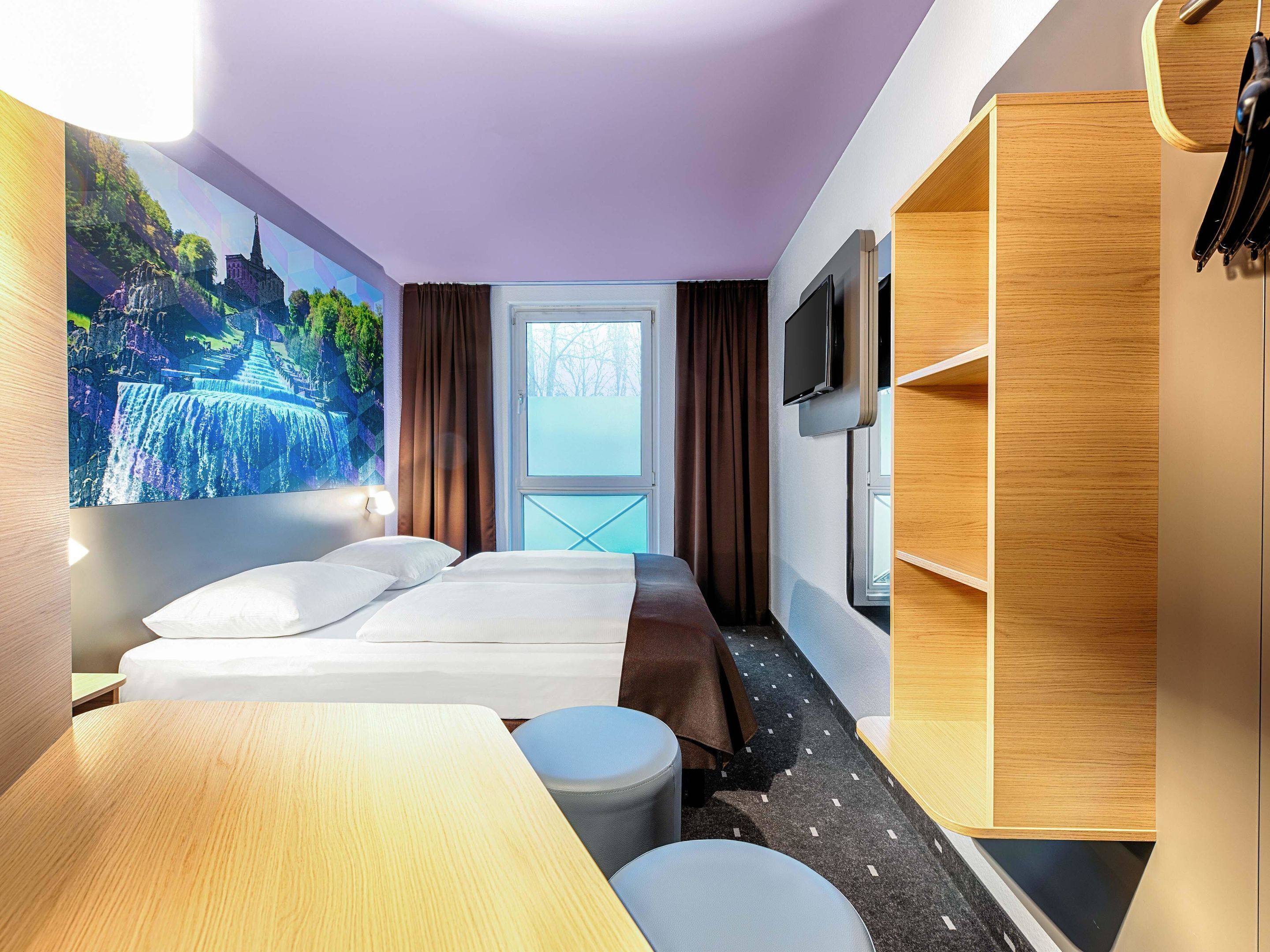 Una habitación de hotel con cama, escritorio, silla, televisor y armario.