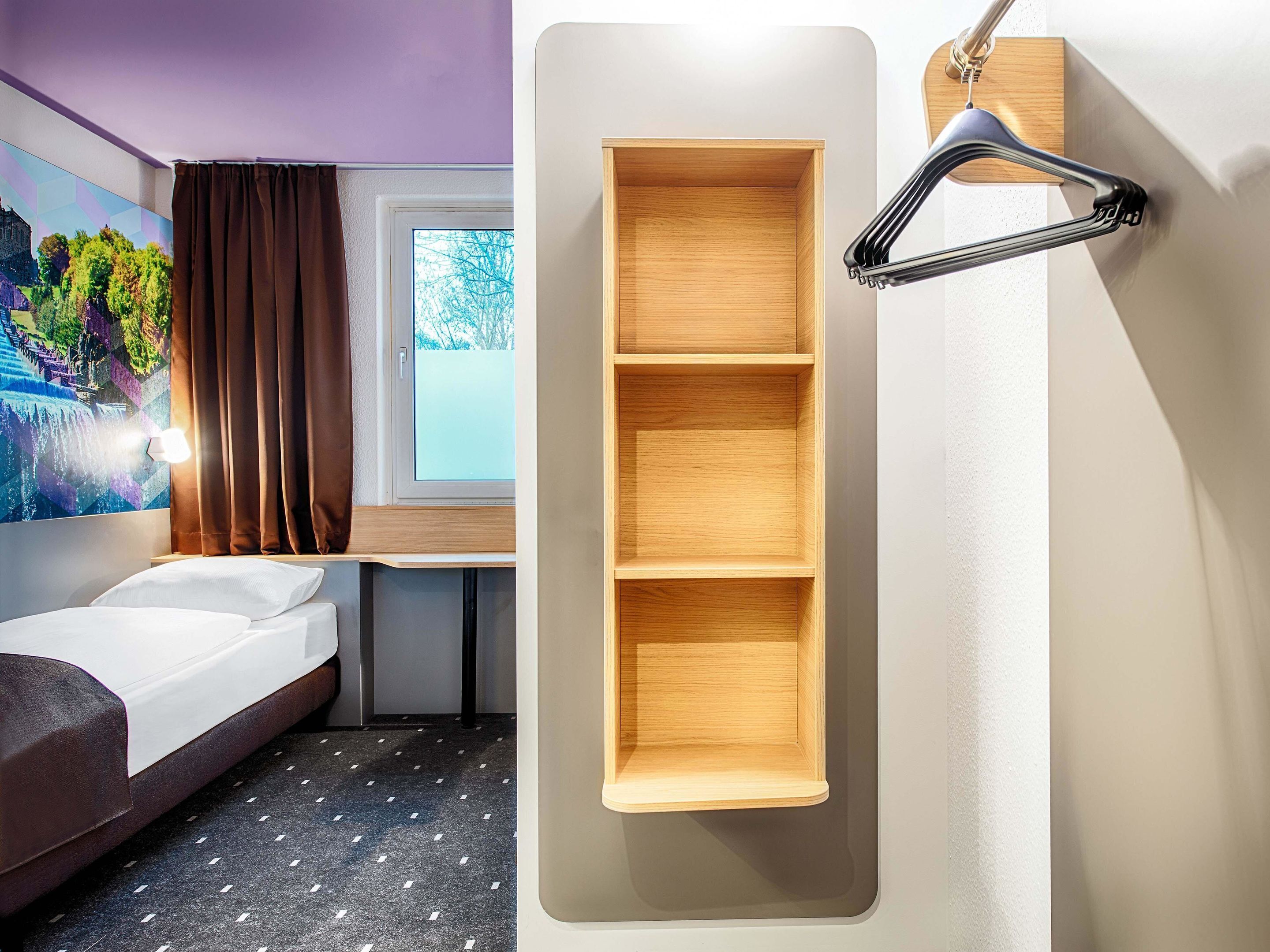 Habitación de hotel con cama, una estantería de madera en la pared y una ventana con cortinas.
