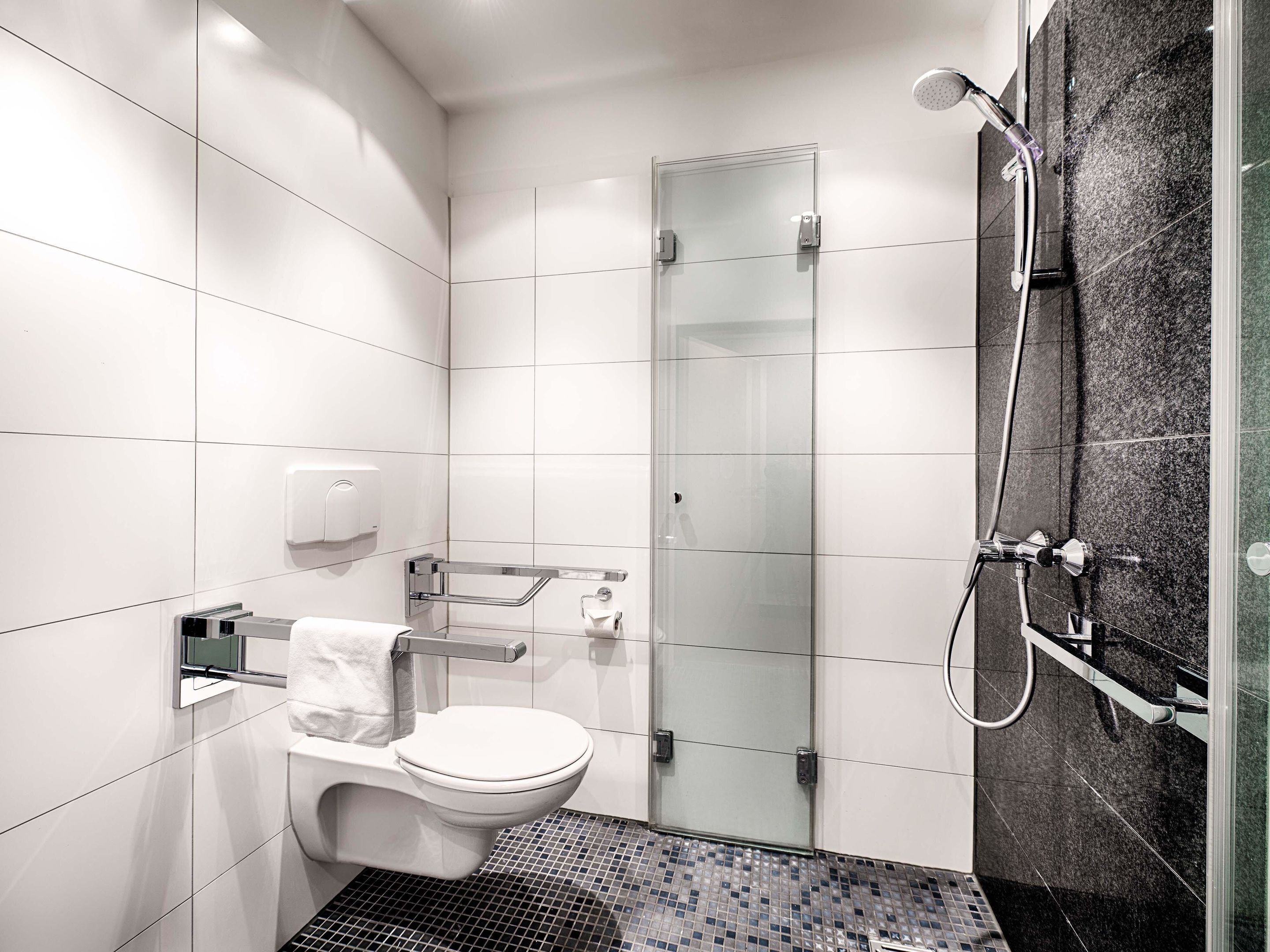 Un baño moderno con inodoro, cabina de ducha de vidrio y secamanos.