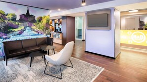 A modern hotel lobby with a reception desk, a seating area with a sofa and chair, a large mural of a castle, and a bar area. - B&B Hotel Kassel-Süd (Lohfelden)
