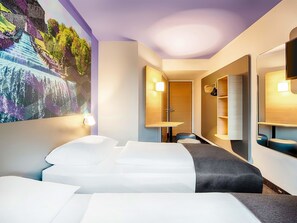 A hotel room with a bed, a desk, a chair, a wardrobe, and a large wall mural. - B&B Hotel Kassel-Süd (Lohfelden)