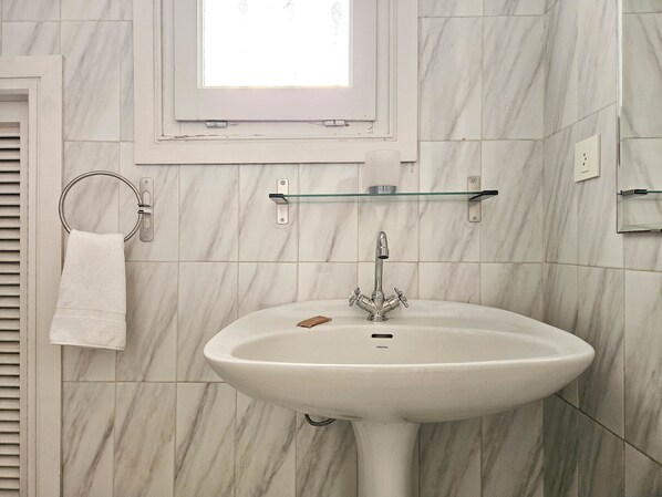 Ein Badezimmer mit einem weißen Waschbecken, einem Handtuchhalter und einer Glasablage.