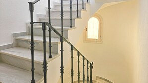 Un escalier avec des balustrades noires et des marches blanches, menant à un palier doté d’une petite fenêtre.
