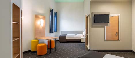 Une chambre d’hôtel comprenant un lit, un bureau, deux poufs orange, un téléviseur fixé au mur et une armoire en bois.