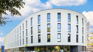 A modern hotel with a curved facade, multiple windows, and a parking lot with various cars.