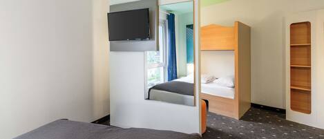 A compact hotel room with a bed, a TV mounted on the wall, a bunk bed, and a built-in shelf.