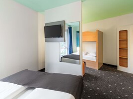 A compact hotel room with a bed, a TV mounted on the wall, a bunk bed, and a built-in shelf.