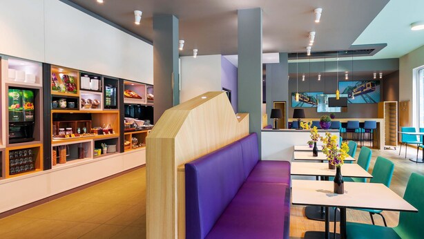 A modern restaurant with a central seating area featuring a wooden partition and purple cushioned benches.