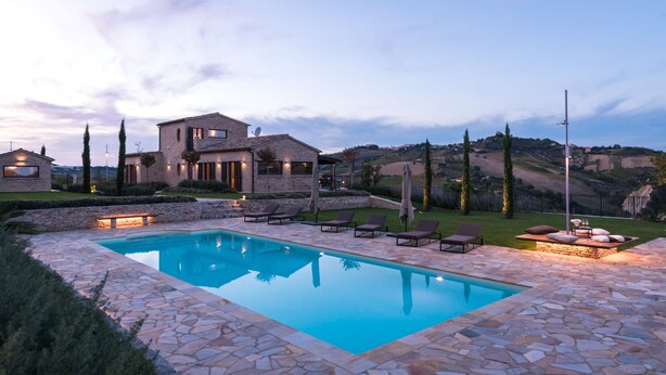 A pool area with stone tiles, lounge chairs, and a stone building with multiple windows. - Borgo Da Monte 8, Emma Villas (Monteprandone)