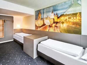 Une chambre d’hôtel moderne avec un grand lit, un petit canapé, un bureau et un téléviseur fixé au mur.