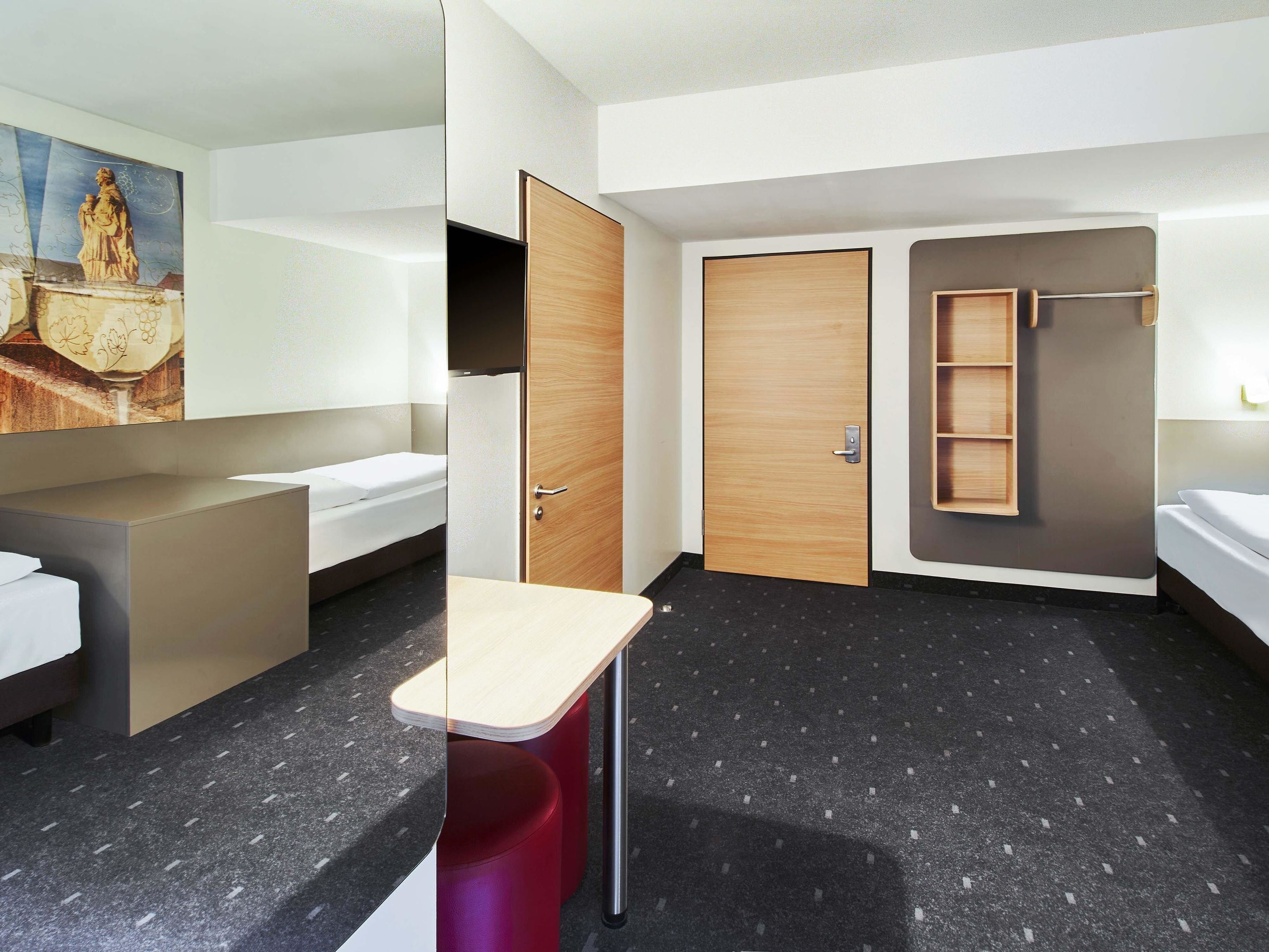 A modern hotel room with a bed, a desk, a wardrobe, and a shower area.