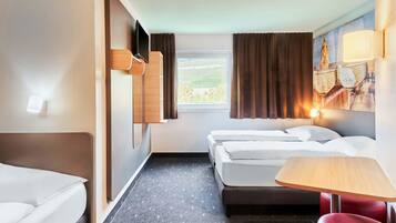 Ein Hotelzimmer mit zwei Betten, einem kleinen Tisch, einem roten Sessel, einem Fenster mit Vorhängen und einem an der Wand befestigten Fernseher.