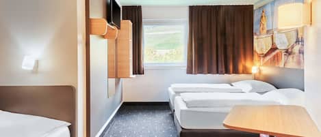 A hotel room with two beds, a small table, a red chair, a window with curtains, and a wall-mounted TV.