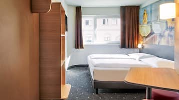 Ein Hotelzimmer mit Bett, Schreibtisch, Stuhl, Kleiderschrank und einem Fenster mit Vorhängen.