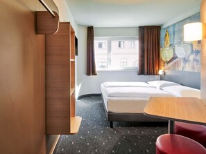 Ein Hotelzimmer mit Bett, Schreibtisch, Stuhl, Kleiderschrank und einem Fenster mit Vorhängen.
