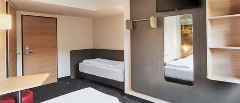 Ett hotellrum med två sängar, en tv som är monterad på väggen, en spegel och en hylla i trä.