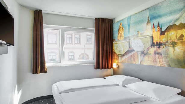 A hotel room with a bed, a window with curtains, a painting of a cityscape, and a wall-mounted TV. - B&B HOTEL Würzburg-City (Würzburg)