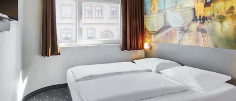 Una habitación de hotel con cama, ventana con cortinas, un cuadro de un paisaje urbano y un televisor instalado en la pared.