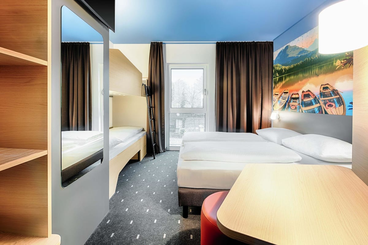 A hotel room with a bunk bed, a desk, and a large window.