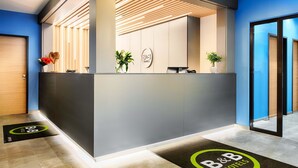 A reception area with a modern design, featuring a reception desk, a plant, and a logo on the wall. - B&B Hotel Kempten (Kempten)