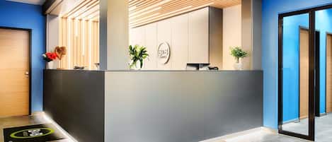 Un área de recepción de diseño moderno, con mostrador de recepción, una planta y un logotipo en la pared.