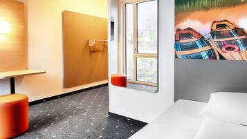 Een hotelkamer met een bed, een raam met uitzicht op boten, een wandplank en een kleine tafel met stoel.