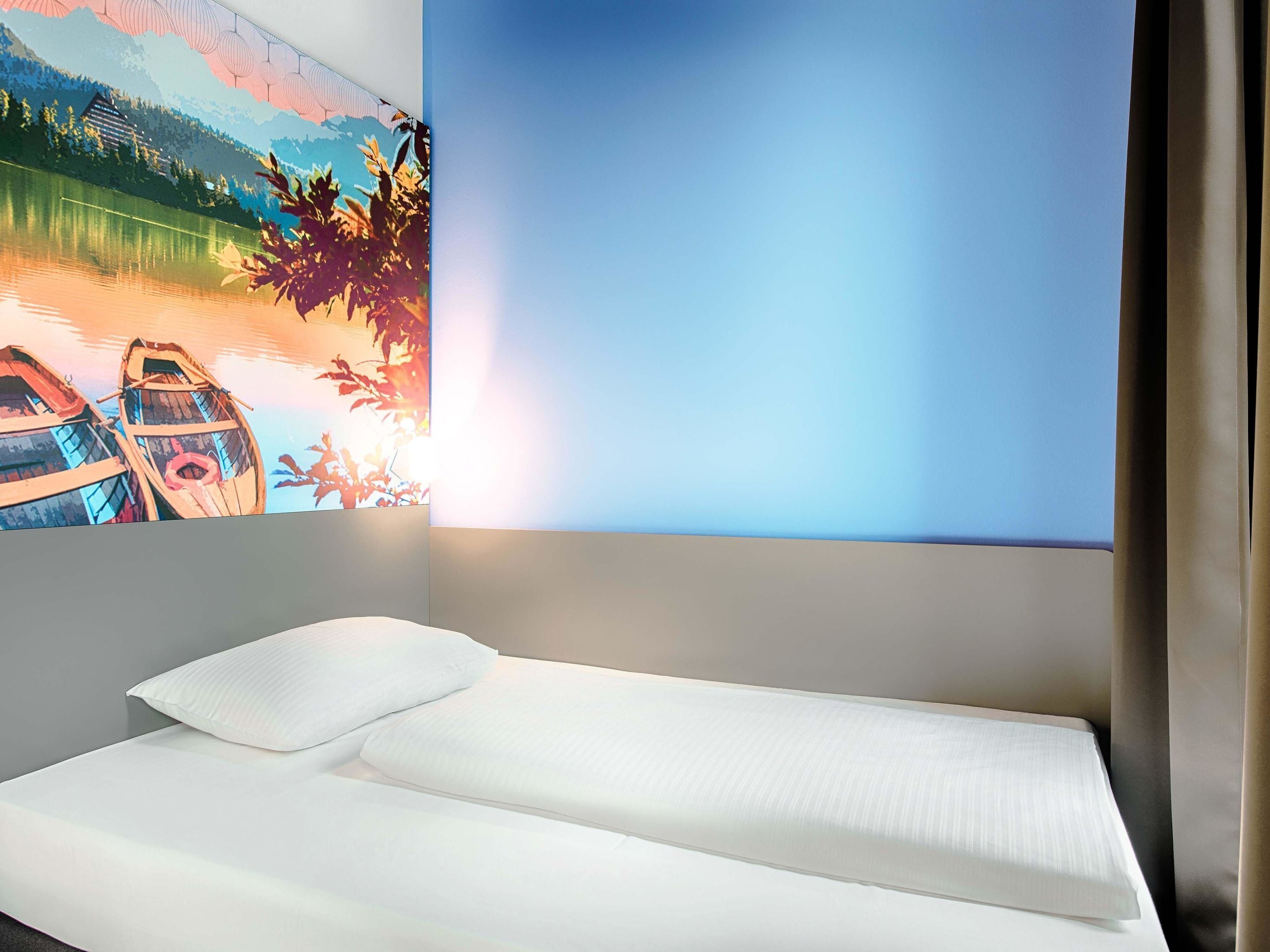 A single bed with white linens in a room with a large wall mural depicting boats on water.