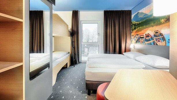 A hotel room with a bunk bed, a desk, and a large window. - B&B Hotel Kempten (Kempten)