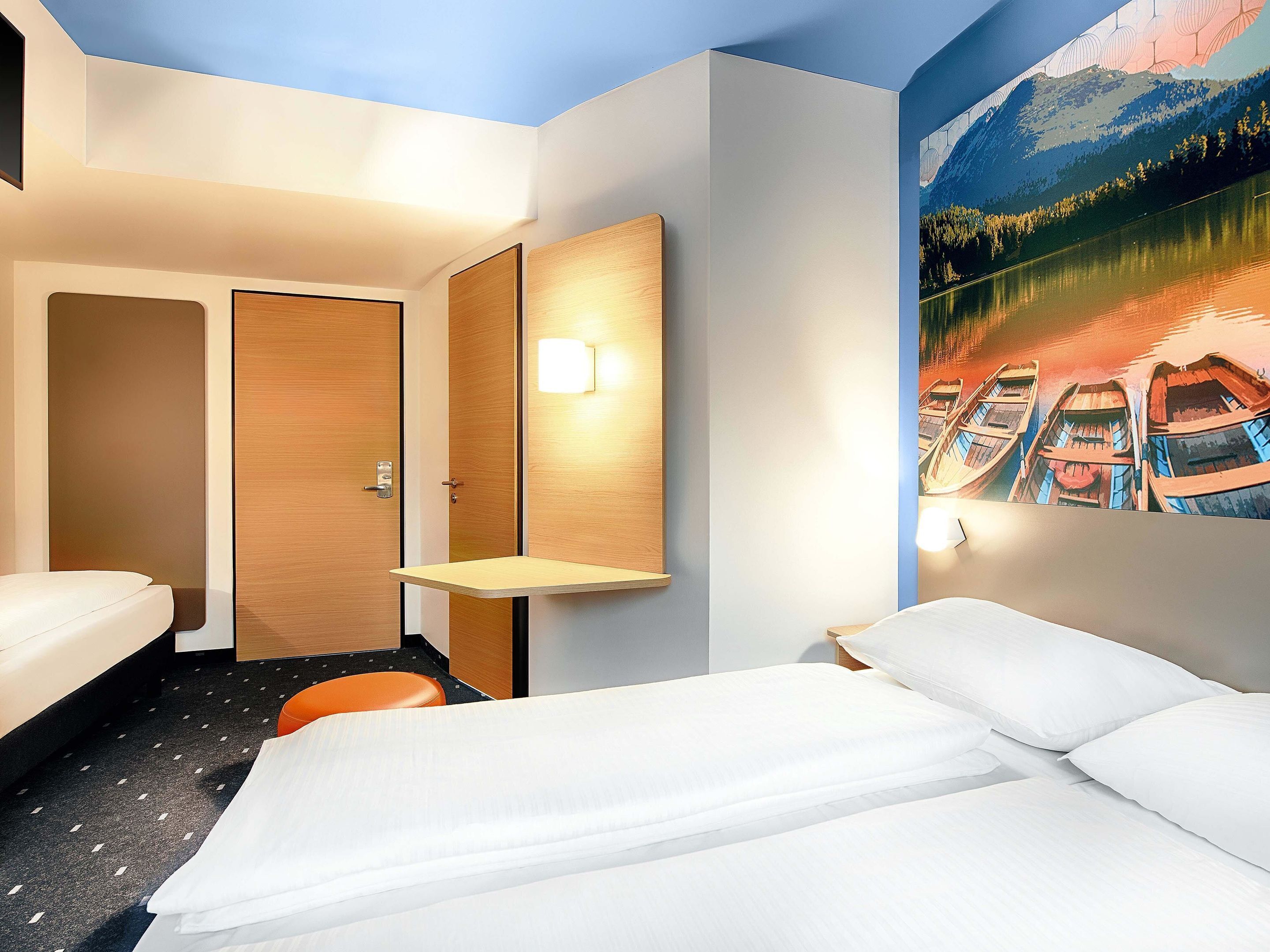 Ein Hotelzimmer mit einem Bett, einem kleinen Tisch, einer Wandleuchte und einem Bild von Booten auf einem See.