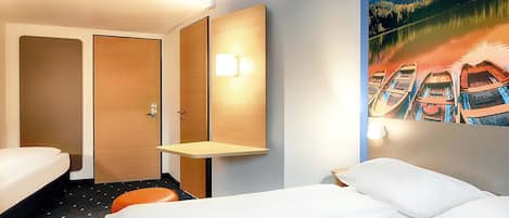 Habitación de hotel con cama, una mesita, una lámpara de pared y un cuadro de barcos en un lago.