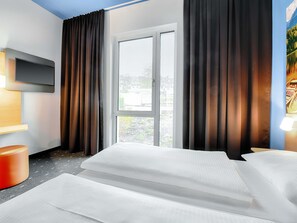 A hotel room with a bed, a TV mounted on the wall, a window with curtains, and a painting on the wall. - B&B Hotel Kempten (Kempten)